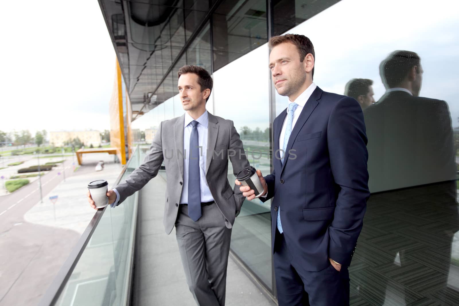 Two business people with coffee chatting on balcony of office building