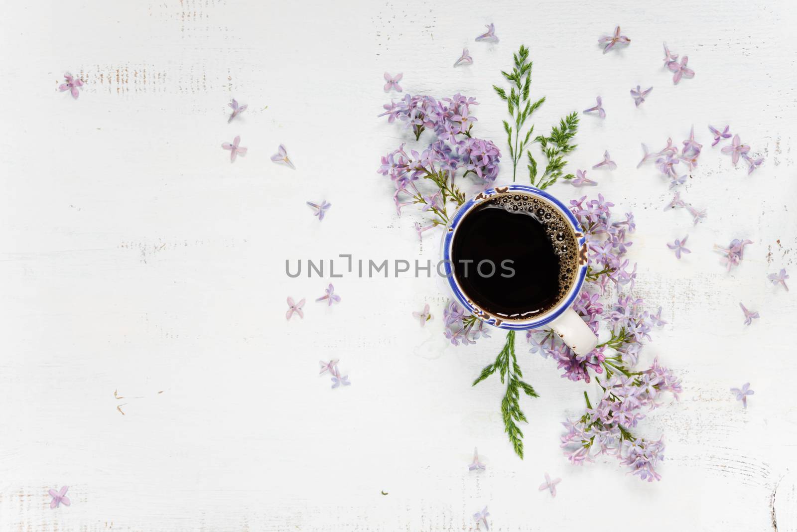 Cup of coffee and purple lilac flowers on the wooden background; flat lay, top view