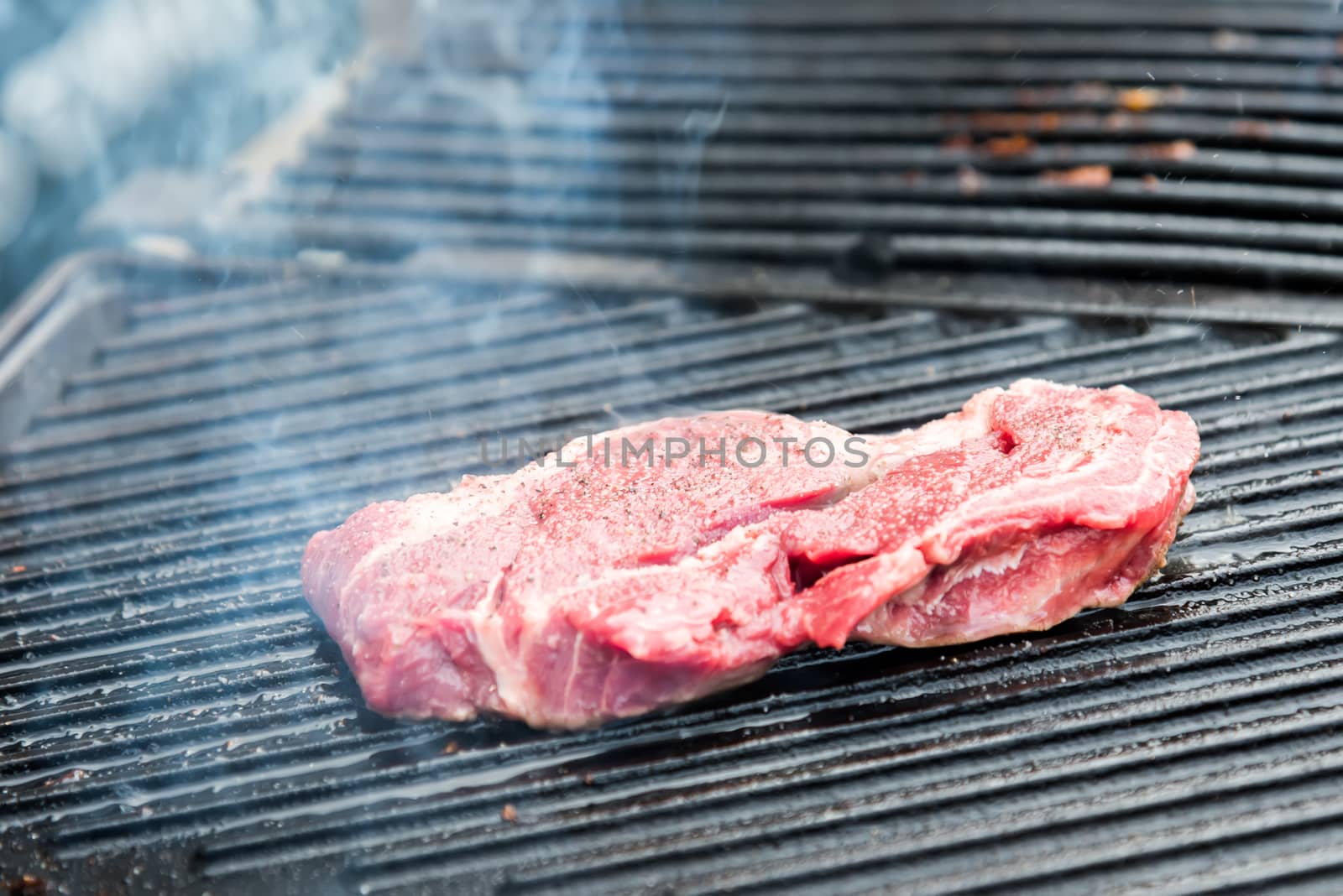 the raw steak with spices on metal grill