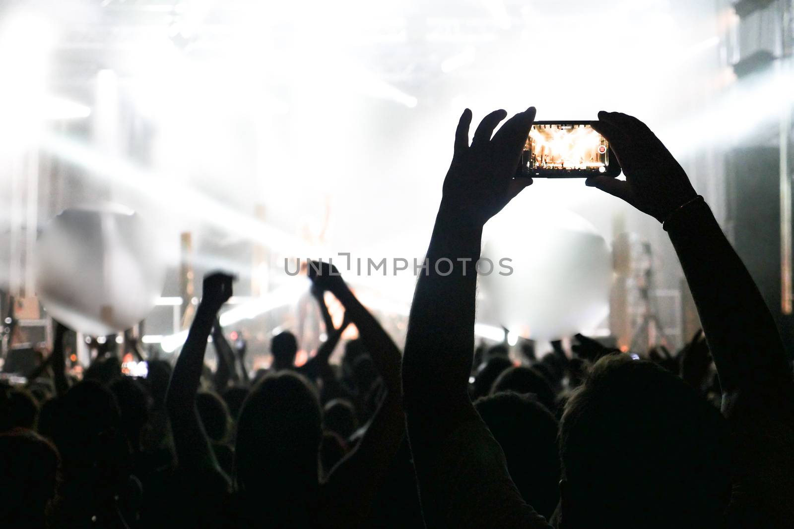 Silhouette of hands recording videos at music concert. Pop music concert with lights, smoke and lots of people