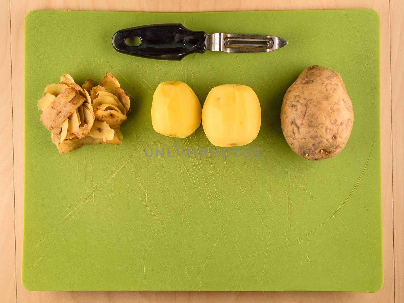Two unpeeled and one peeled potatoes with skins on green plastic board with peeler, simple food preparation illustration, vegetarian dieting, top view still life with bottom half copyspace
