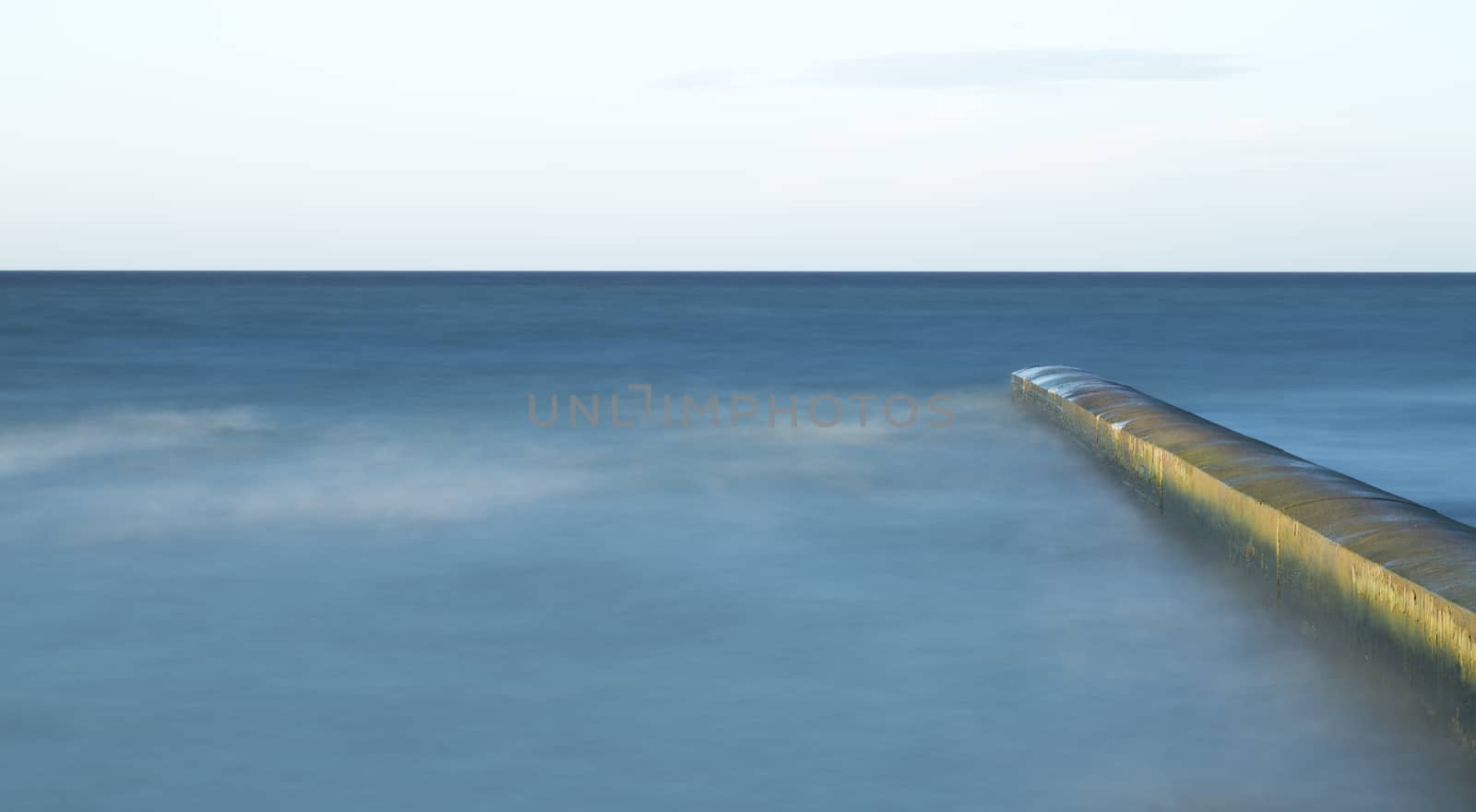 Calm Ocean with Breakwater Structure with clouds in the sky.