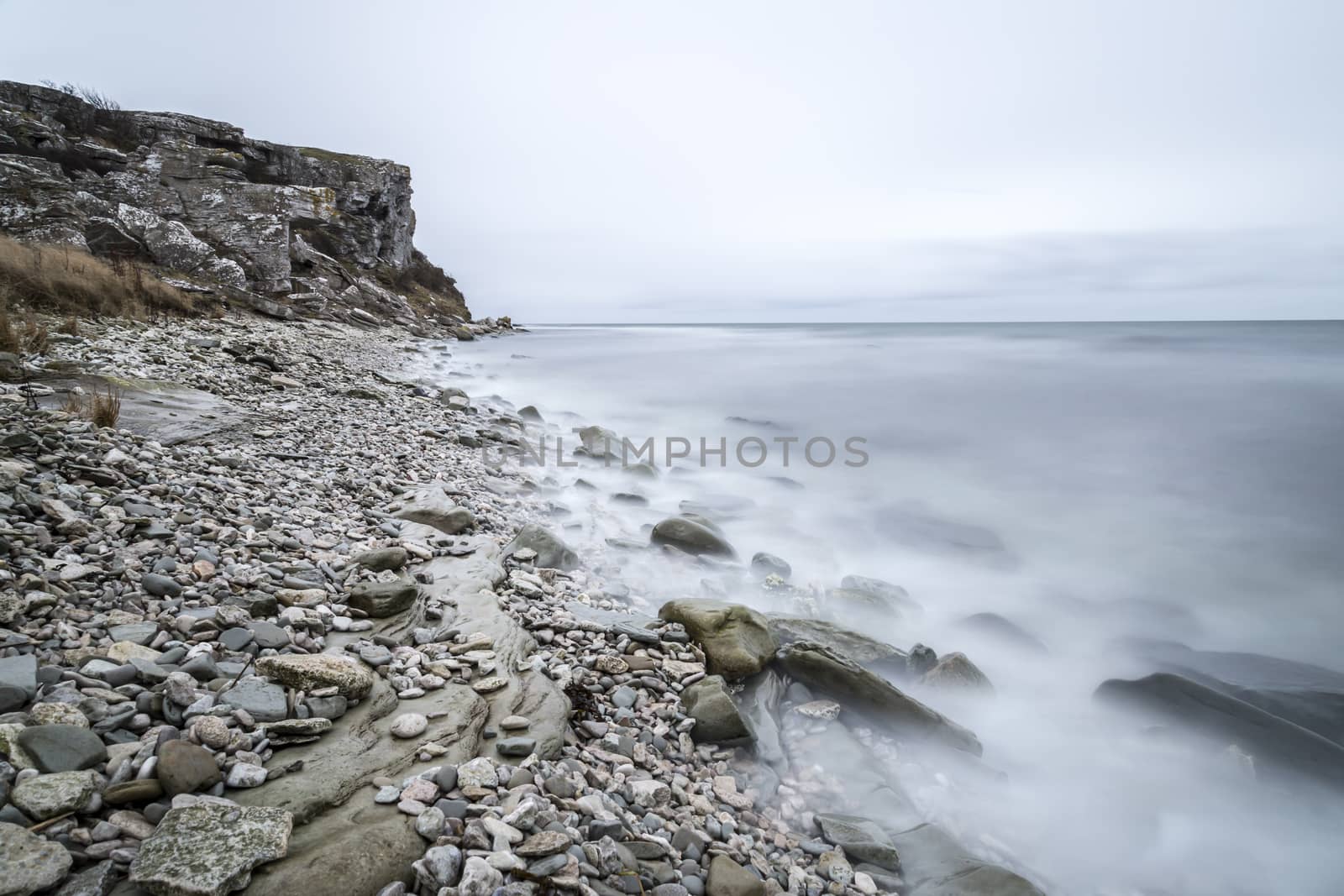 Rocky Shore by Ocean with cliff and a cloudy sky.