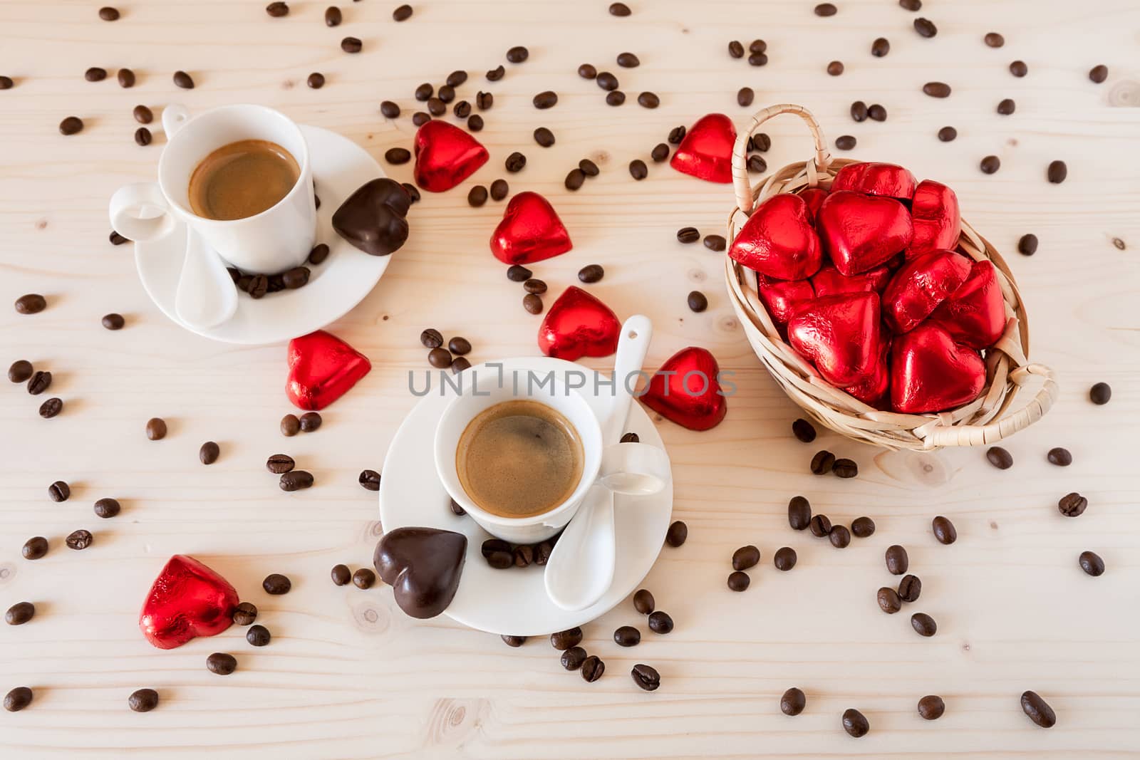 Red chocolate hearts in a small basket and two cups of coffee with coffee beans viewed from above