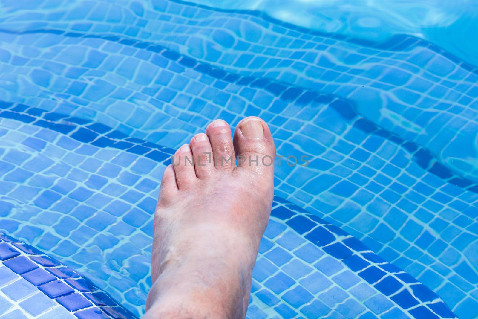 Men feet in a beautiful swimming pool with blue tiles.