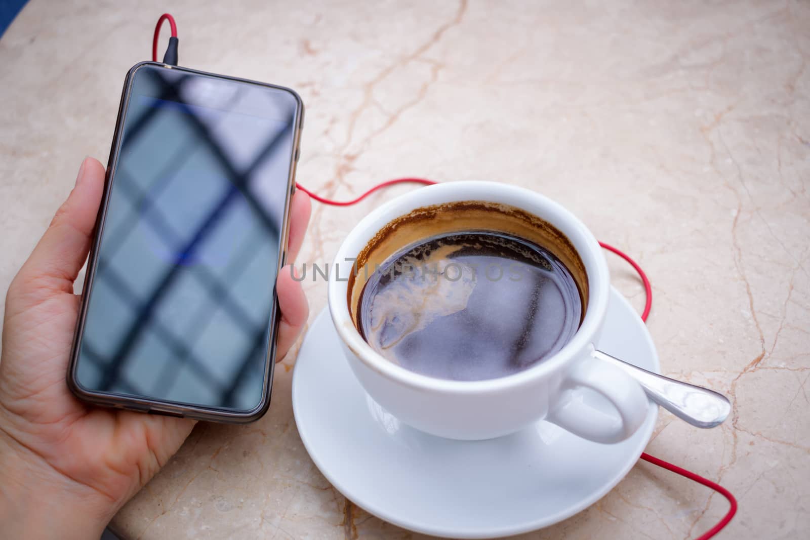 Smartphone at hand and americano coffee in white cup at marble table top