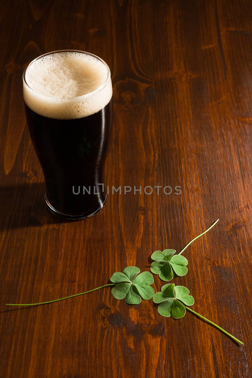 Pint of black beer and three shamrocks on a wood background.