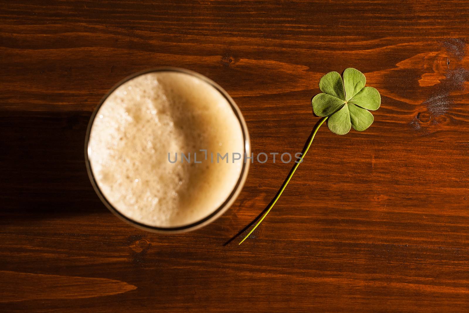 Pint of black beer and a shamrock on a wood background seen from above.
