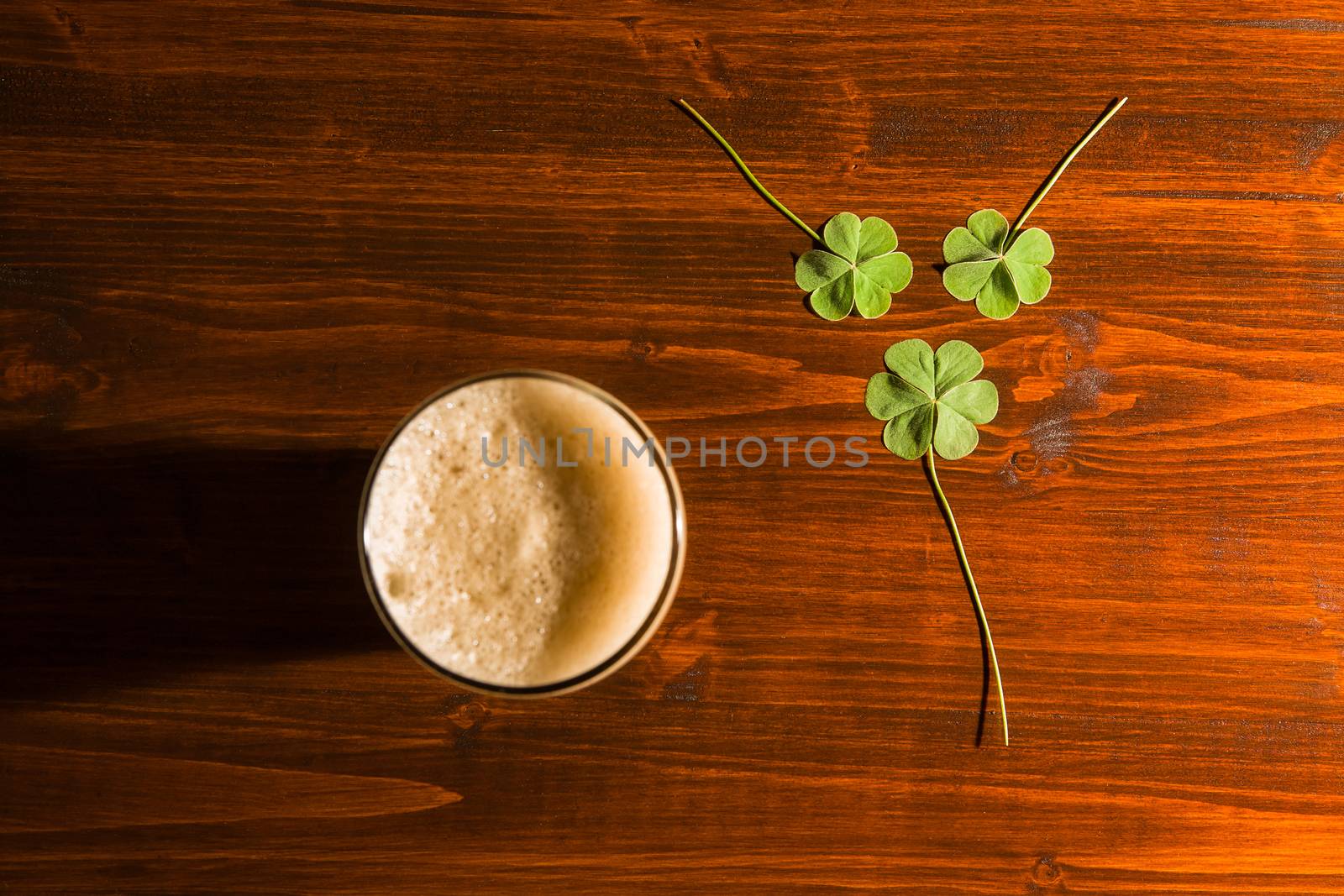 Pint of black beer and three shamrocks on a wood background seen from above.