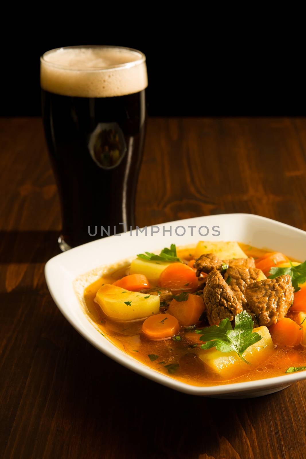 Traditional Irish Stew on a square plate with a pint of beer on a table.