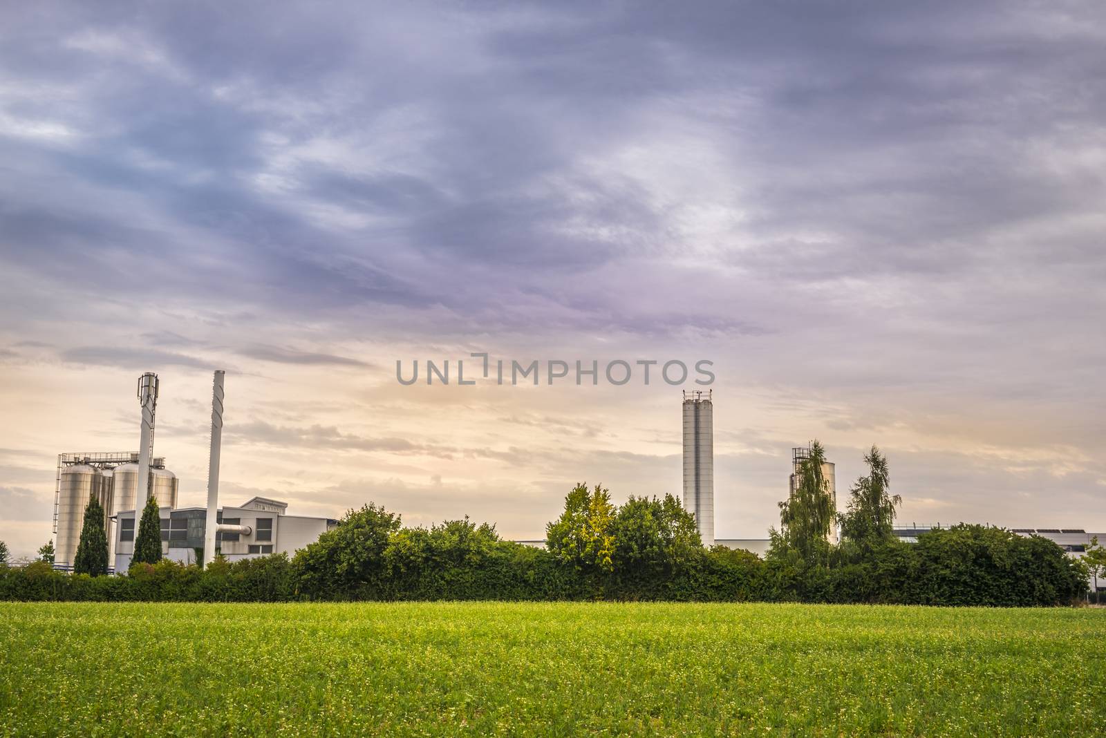 Image with an electric power plant with all its units, in the middle of green vegetation, under a dramatic sky.