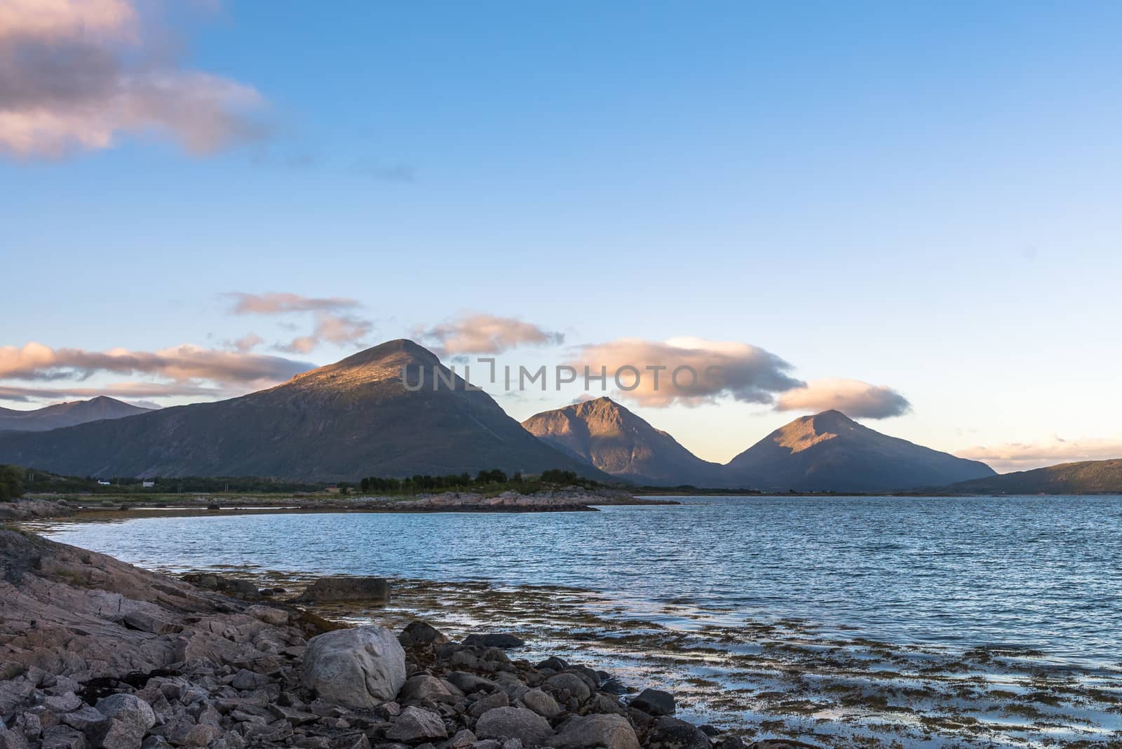 Summer landscape with rocky shore and sharp mountain peaks in Norway.