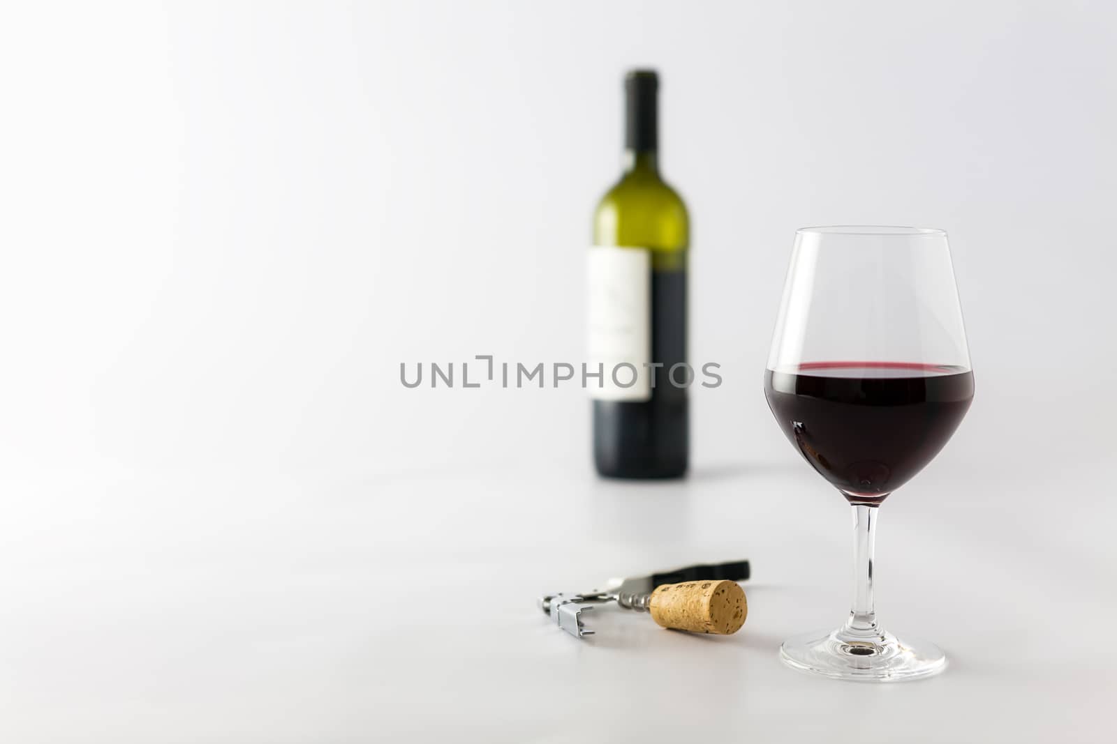 Glass of red wine and bottle on a white background with cork and corkscrew