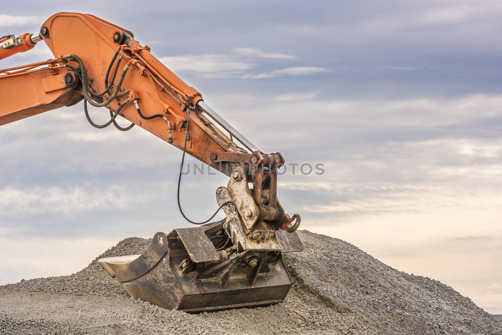 Close up with the details of an orange excavator arm and bucket in a pile of ballast