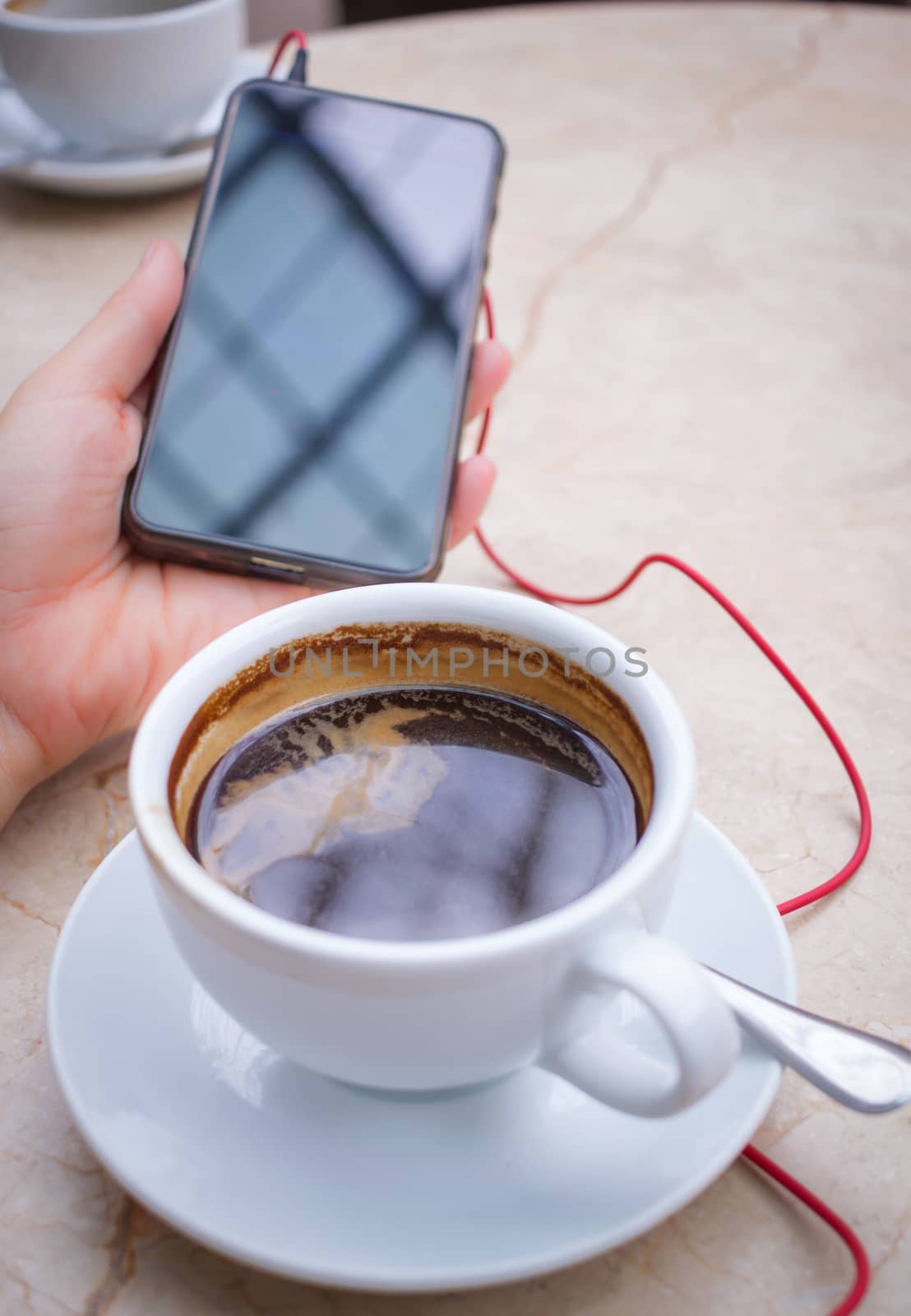 Smartphone at hand and americano coffee in white cup at marble table top