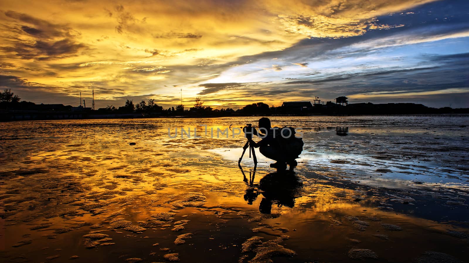 Silhouette of Asian photographer take photo with nature background, vibrant yellow of sky in sunset, wonderful landscape for Vietnam travel, tide going out at sea