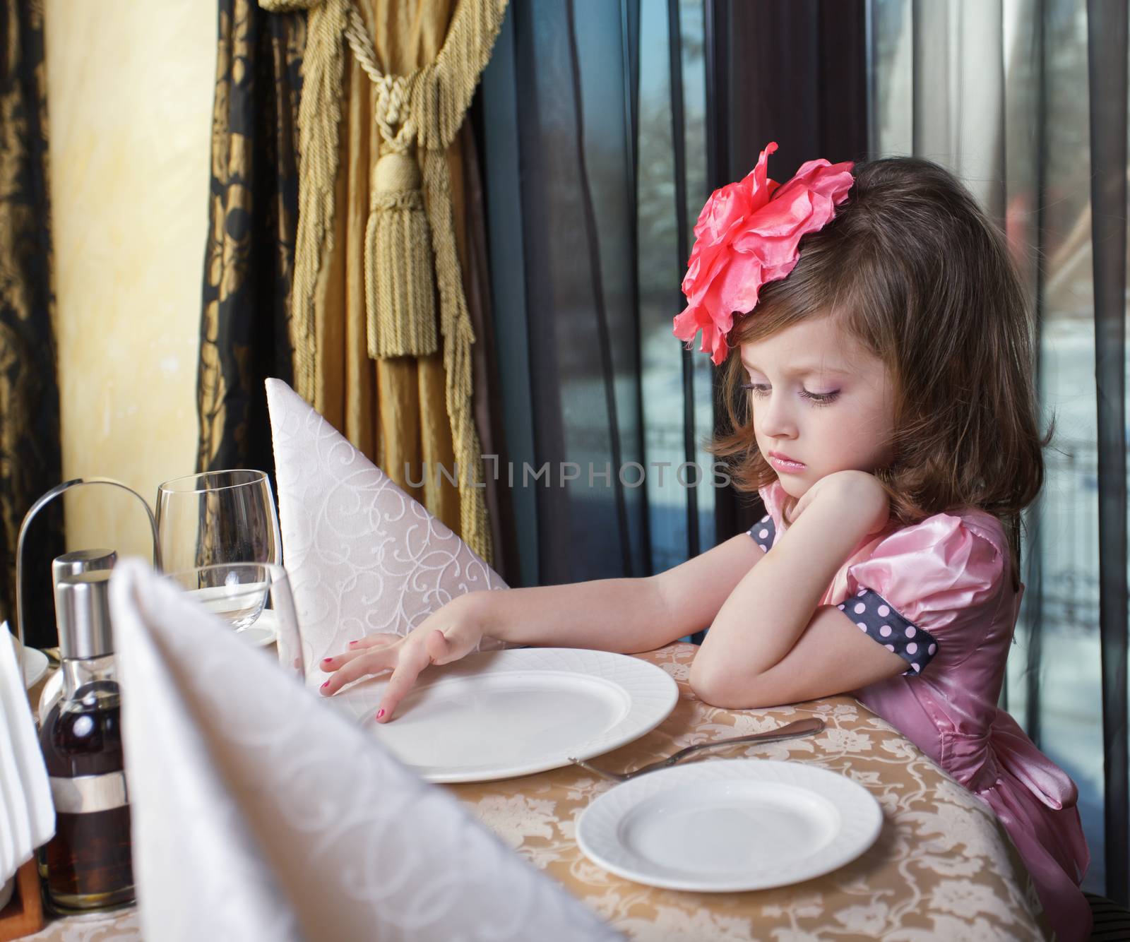 A girl in a pink dress, sad at the table waiting for food