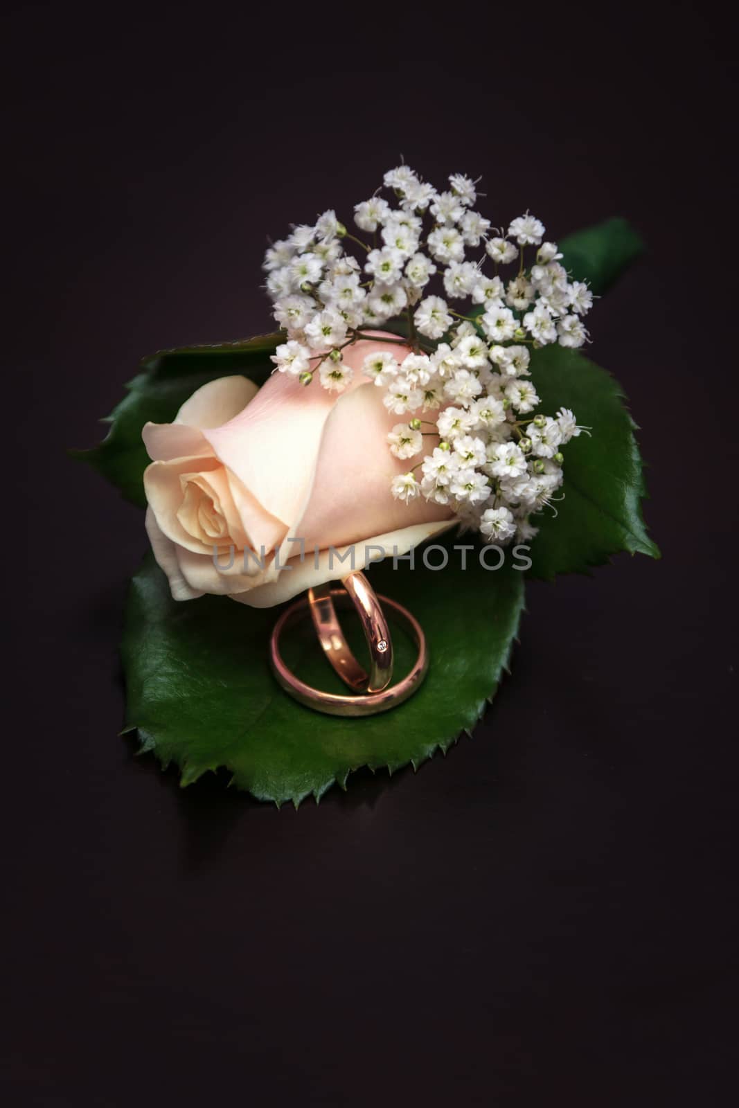 Wedding rings and pibk boutonniere lie on the brown background