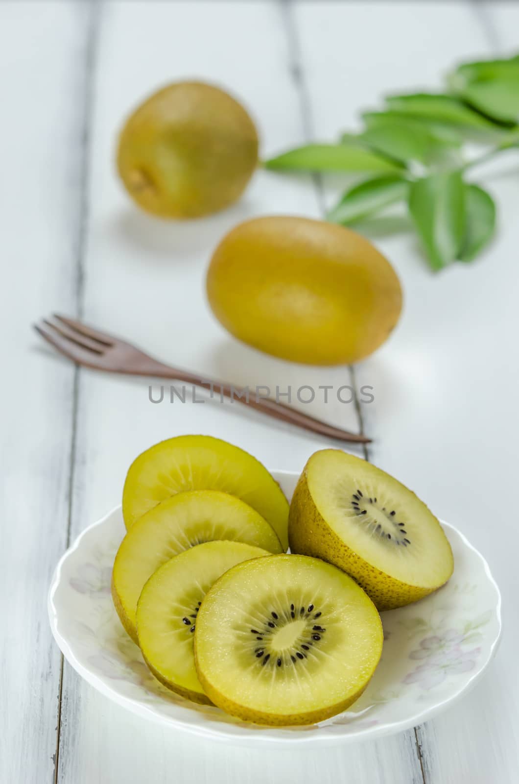 golden kiwi fruit and sliced on dish over white wooden background