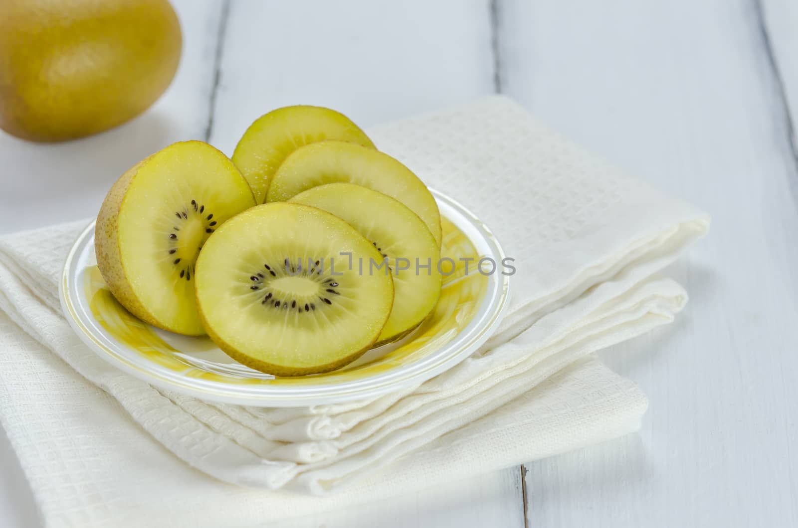golden kiwi fruit and sliced on dish over white wooden background