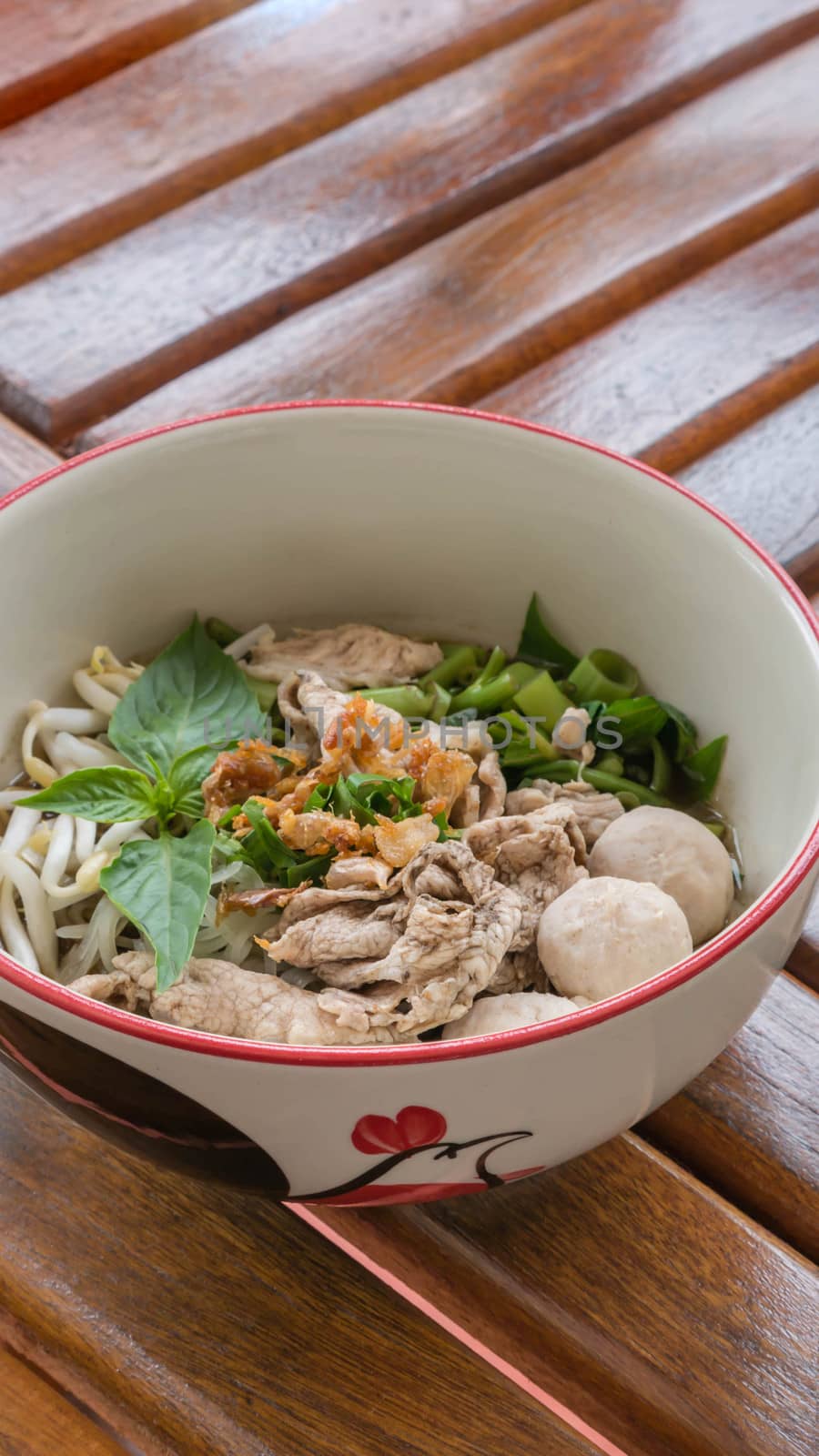 Asian white noodles with pork and vegetables in bowl over wooden background