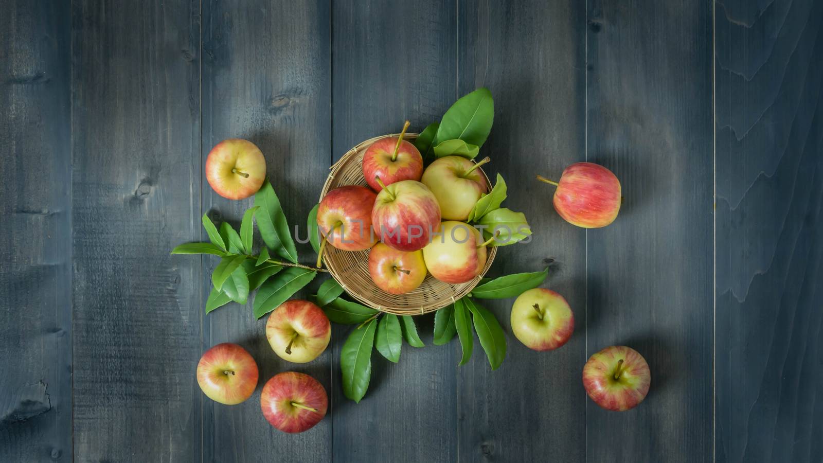 Top view red and yellow apple with leaves and  bamboo basket on wooden background with free space for text
