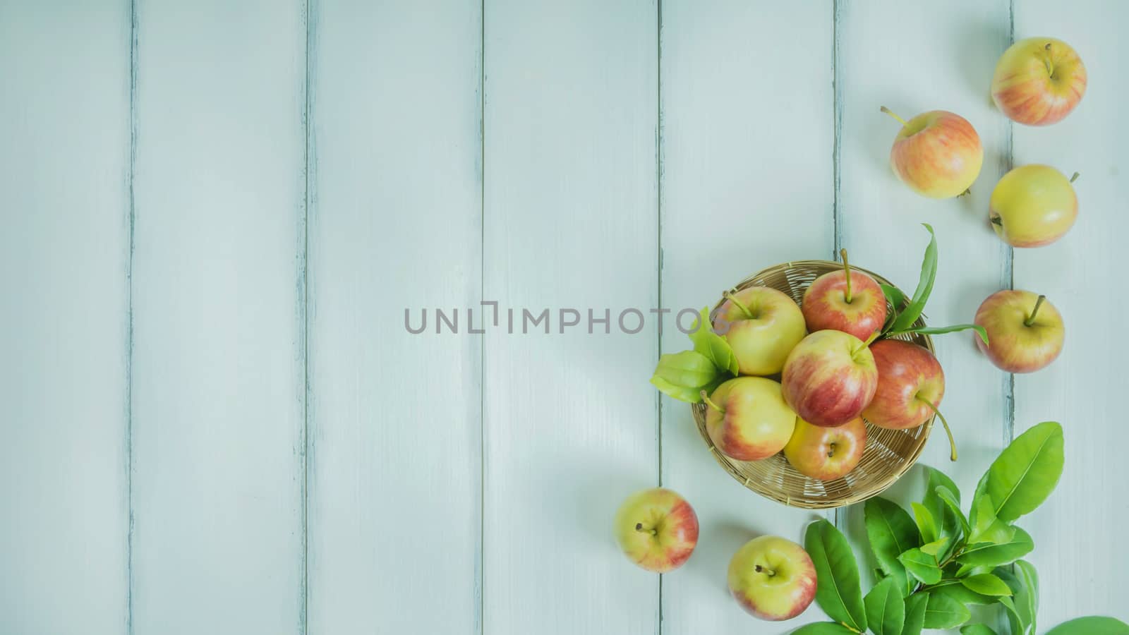 Top view red and yellow apple with leaves and  bamboo basket on  white wooden background with free space for text