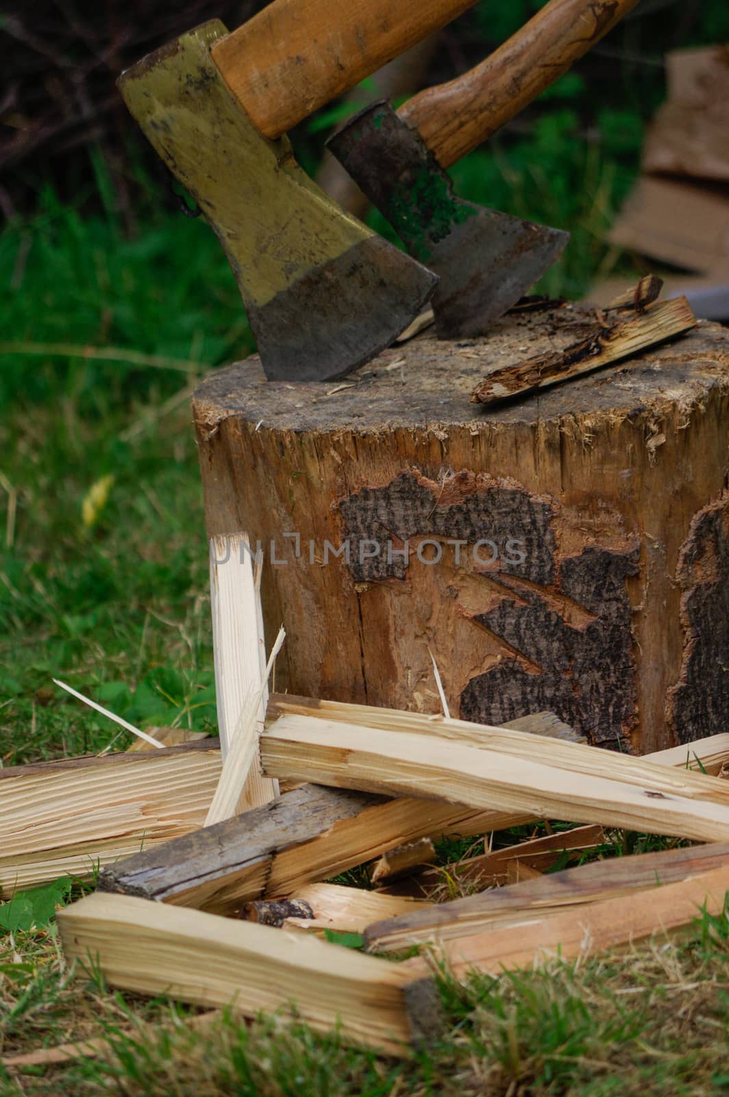 Ax in the deck on a background of green grass and firewood