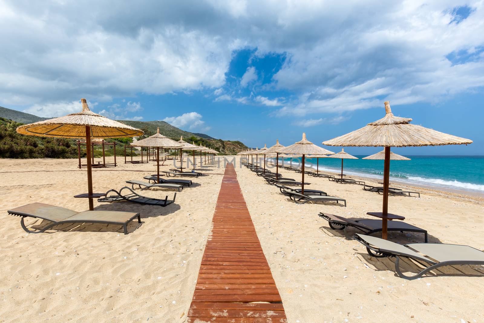 Beach umbrellas and bedchairs near path at greek sea