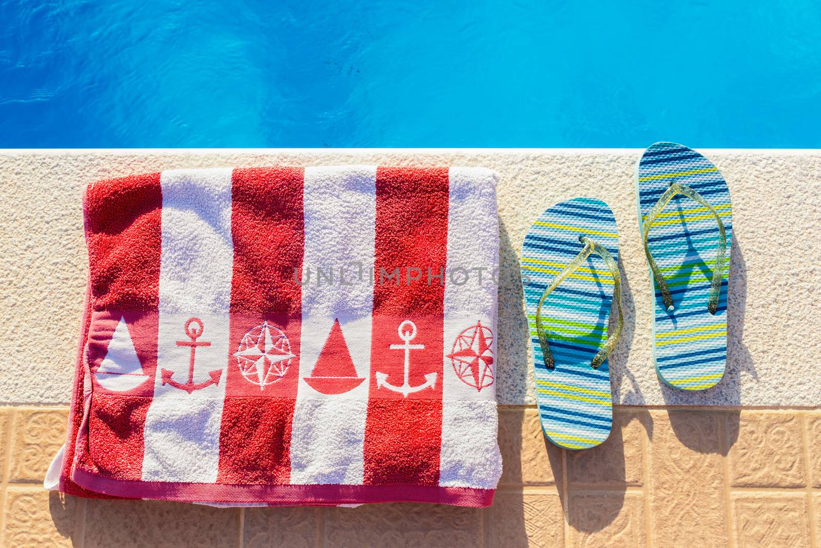 Bathing slippers and bath towel at blue swimming pool in summer