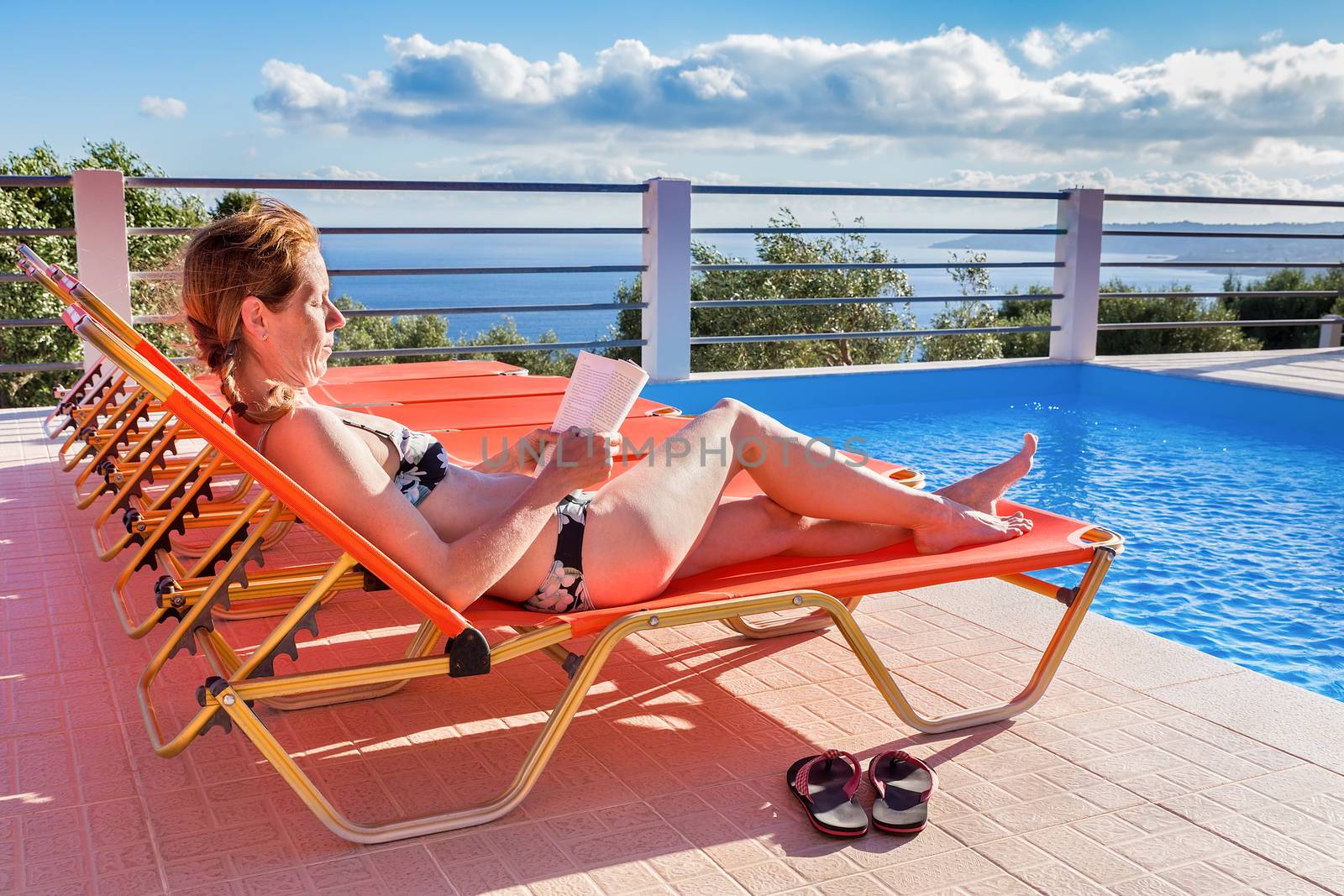 Caucasian woman sunbathing and reading book near swimming pool