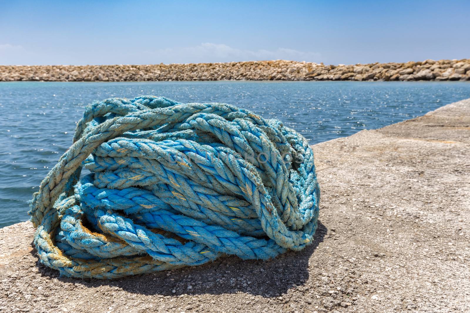 Coiled blue mooring rope at water in greek cave by BenSchonewille