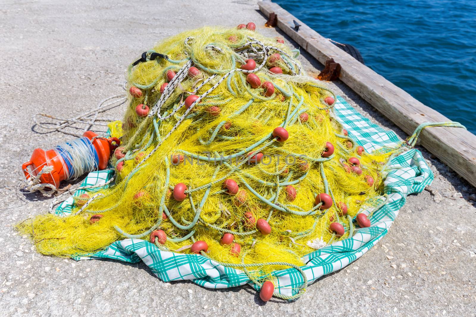 Heap of yellow fishing net with orange floats on ground at  ocean