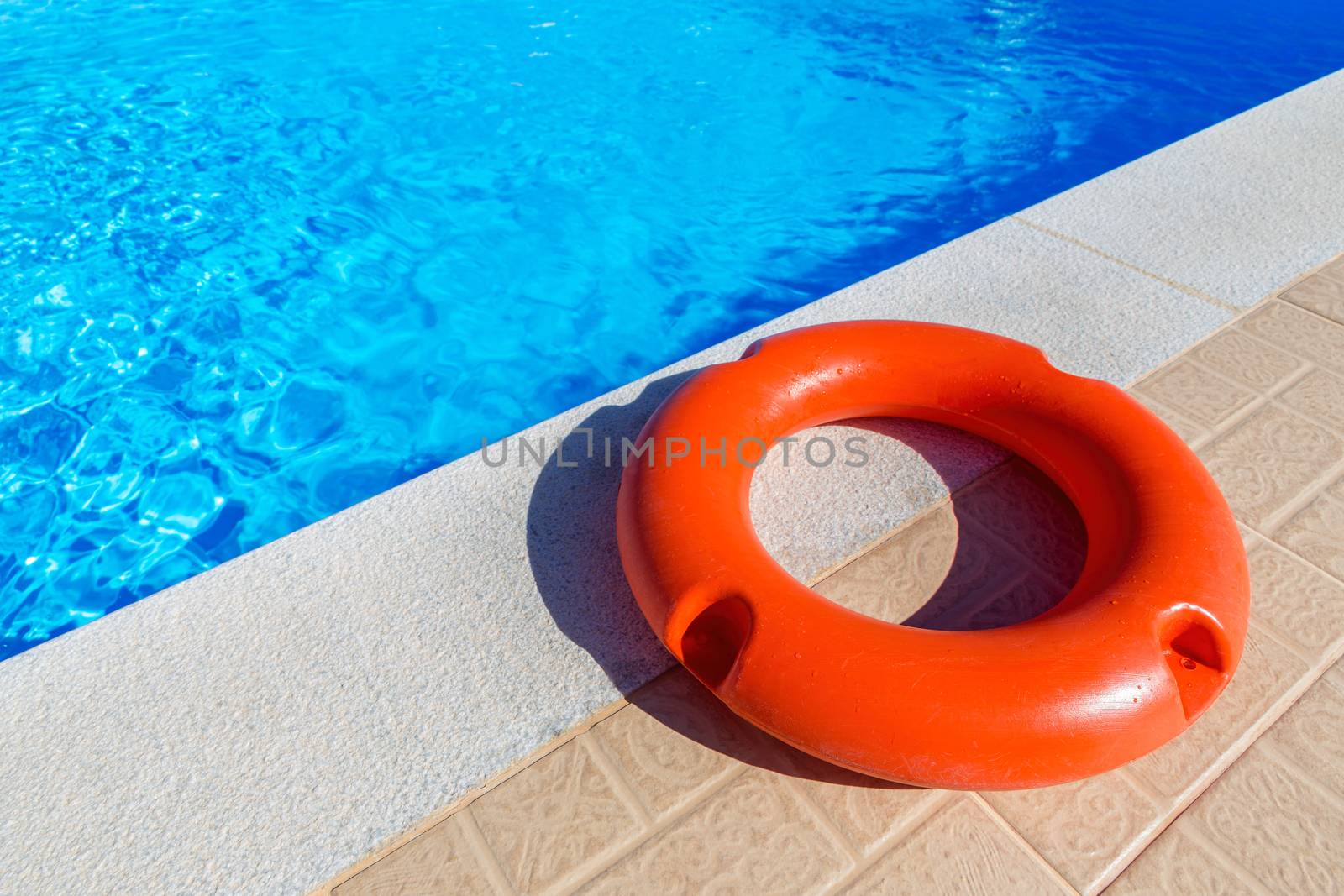 Orange life buoy lying at blue swimming pool