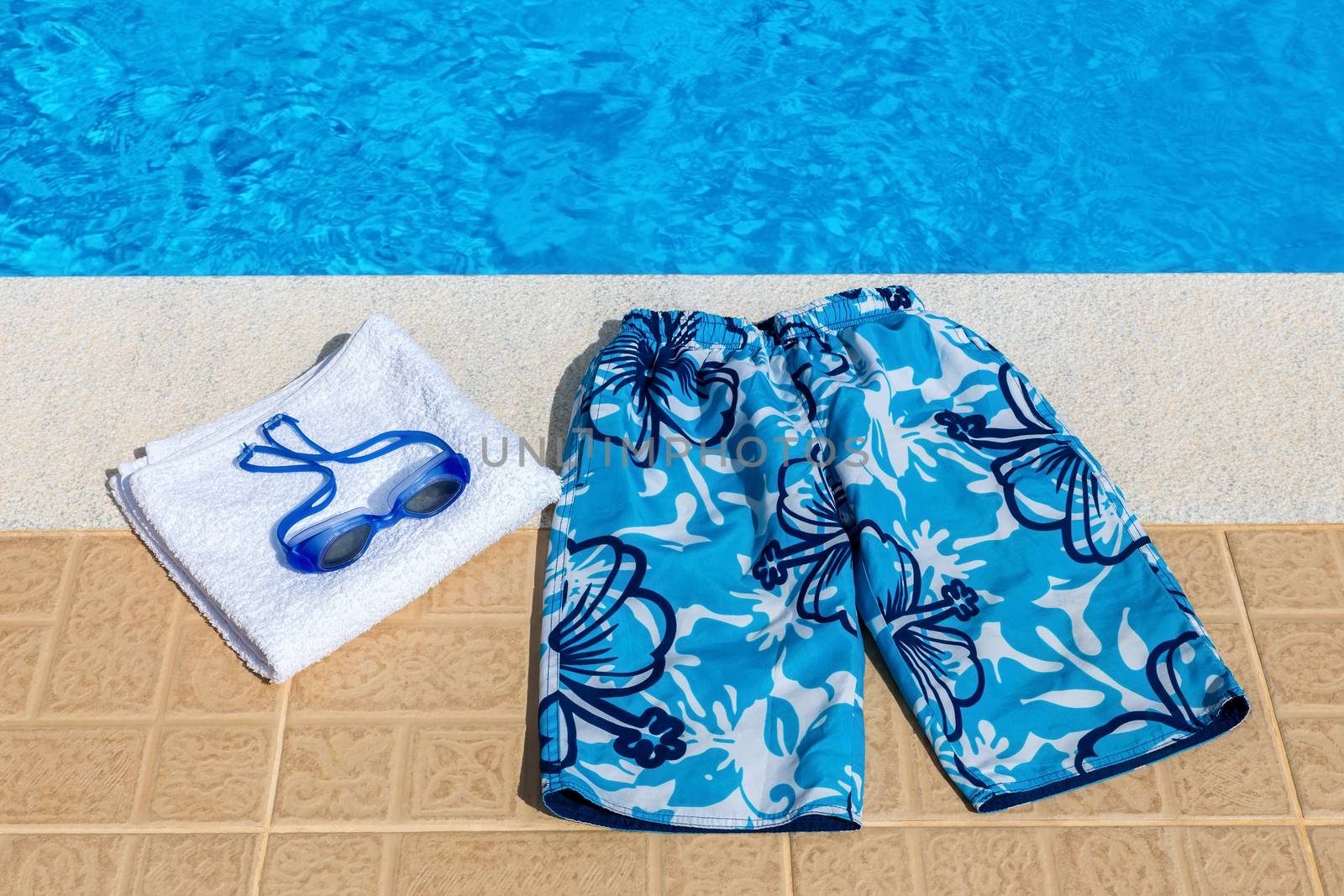 Swimming trunks goggles and towel at pool by BenSchonewille