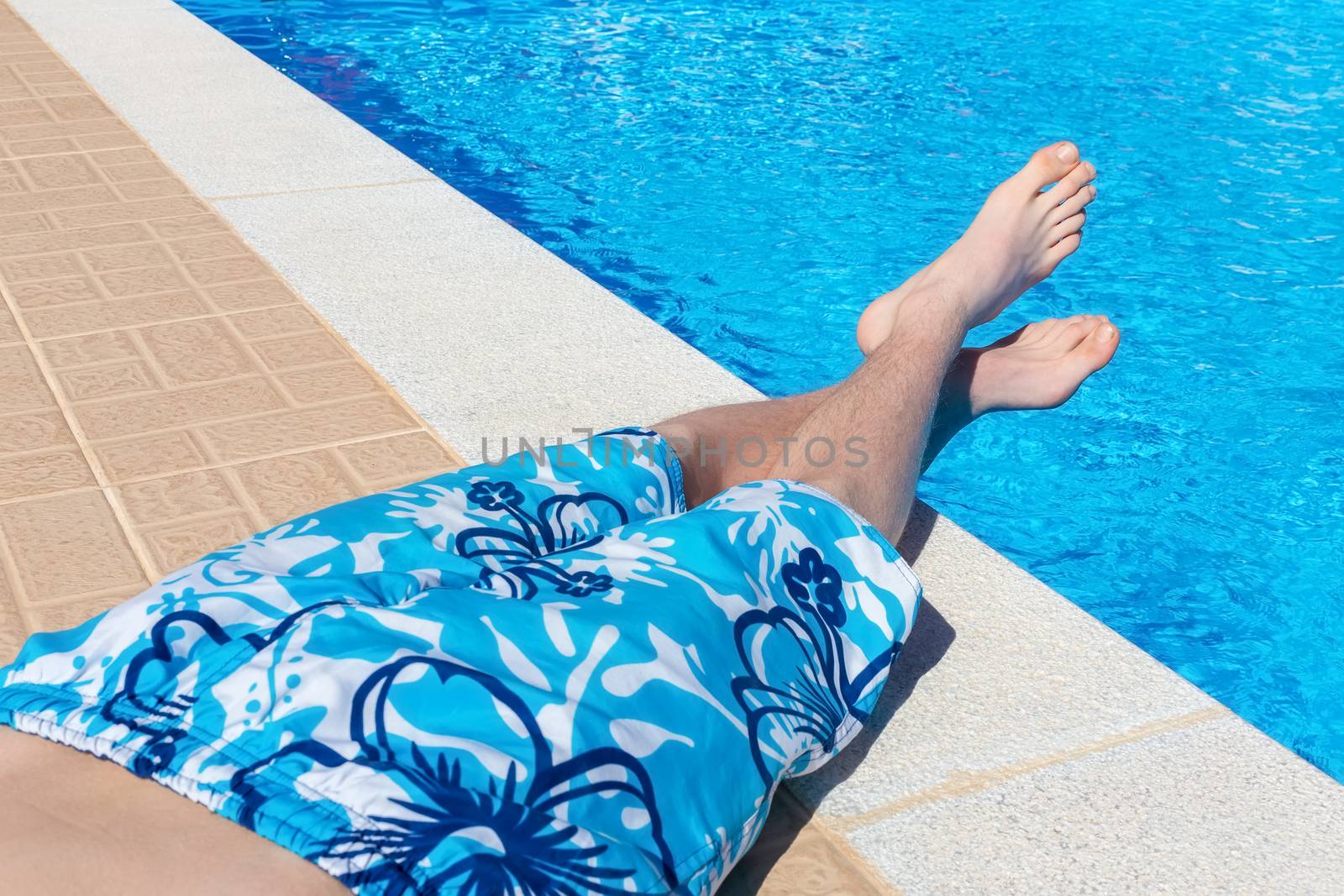 Teenage boy sunbathing at blue swimming pool on vacation in summer season