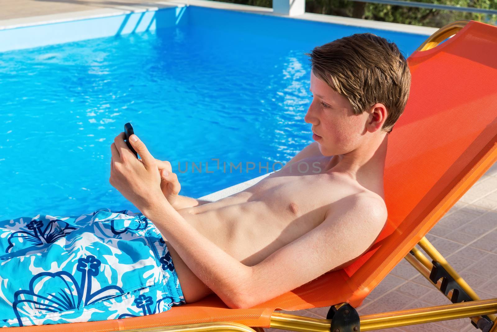 Youngster operating mobile phone at swimming pool by BenSchonewille