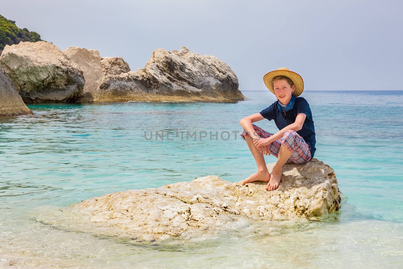 Caucasian teenage boy with hat sitting on rock in sea water