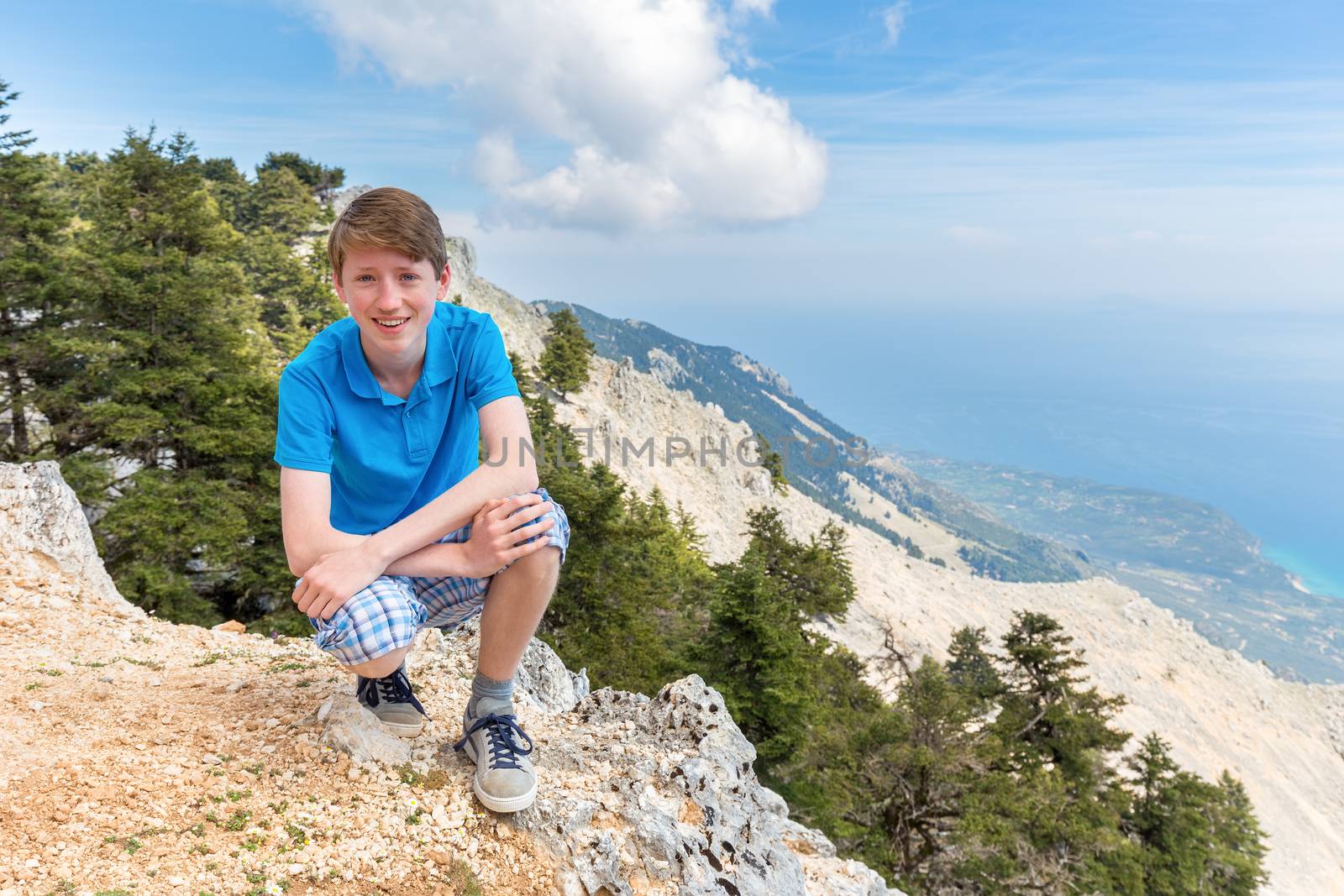 European teenage boy high up in mountains with coast and sea