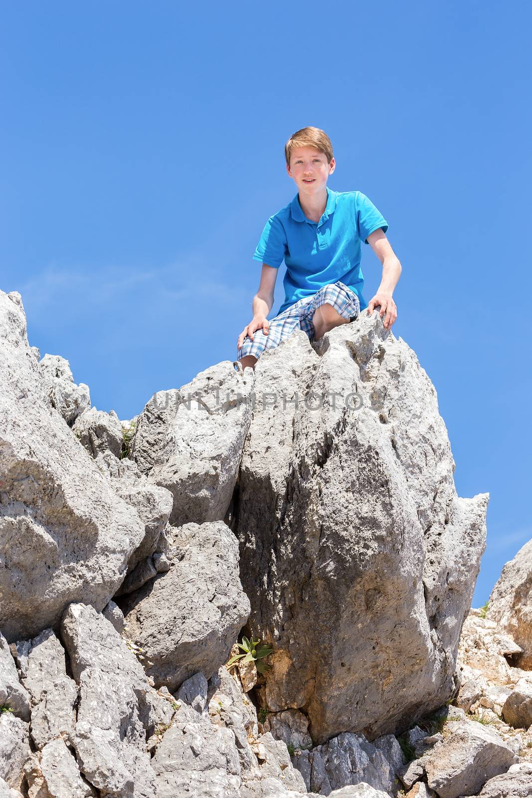 Caucasian teenage boy sitting on top of rocks with blue sky