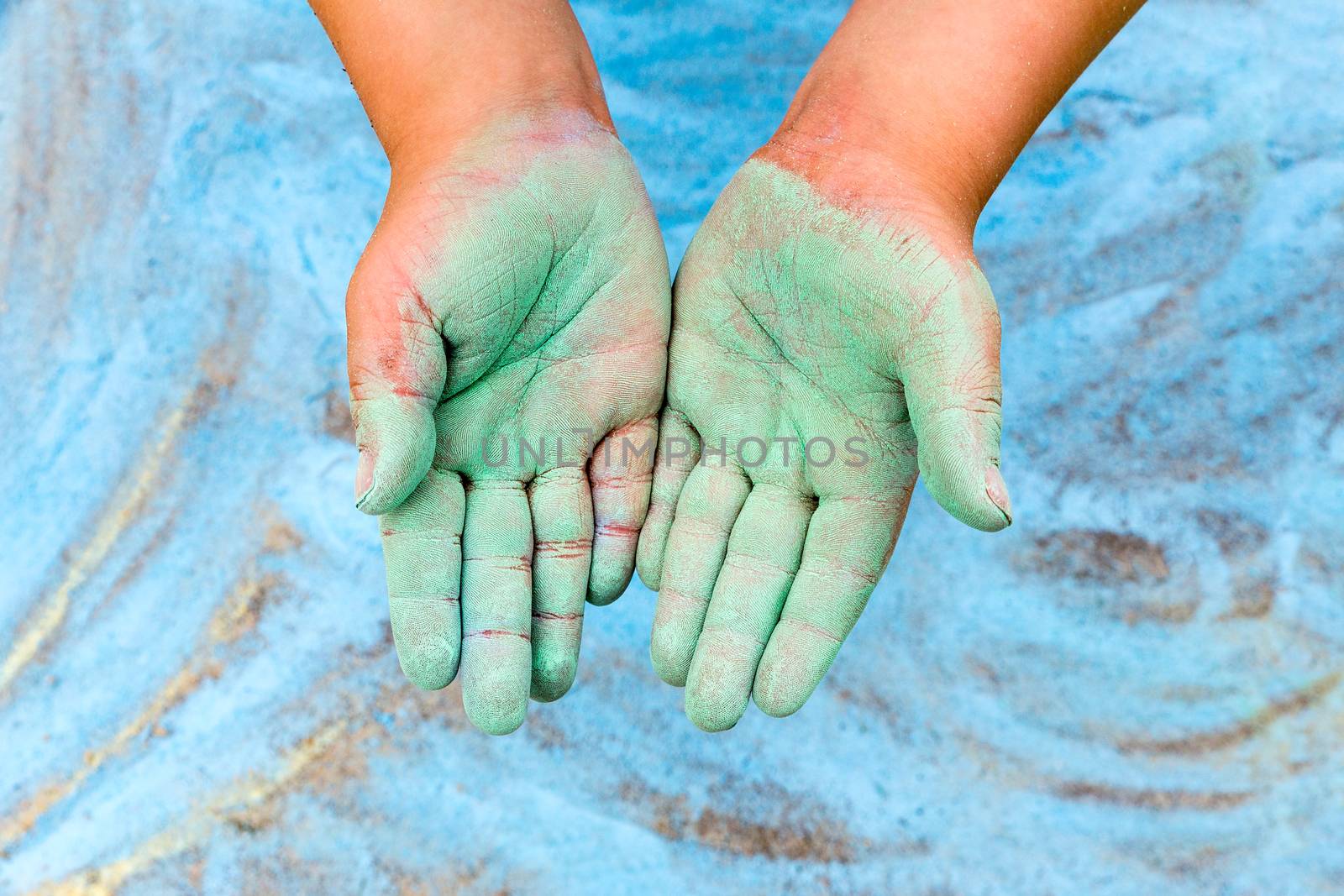 Toddler showing green hands with chalk on blue background