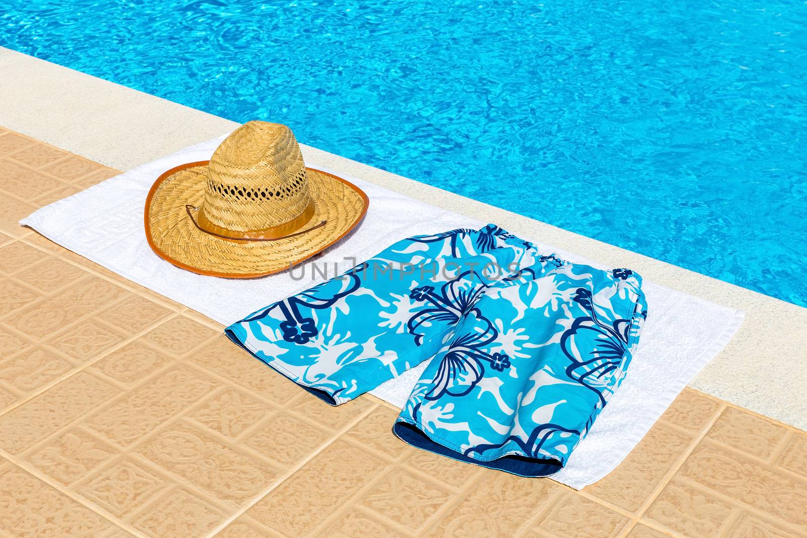 reed hat and swimming trunks on towel near blue fswimming pool