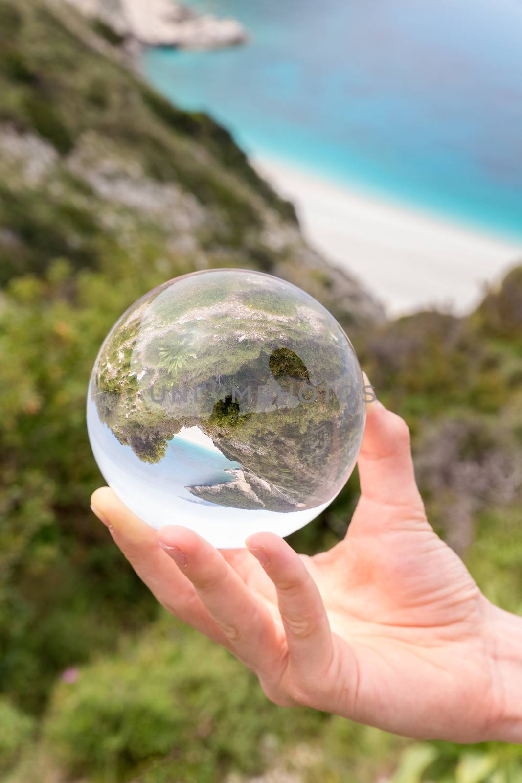 Hand holding crystal ball near sea beach and mountain
