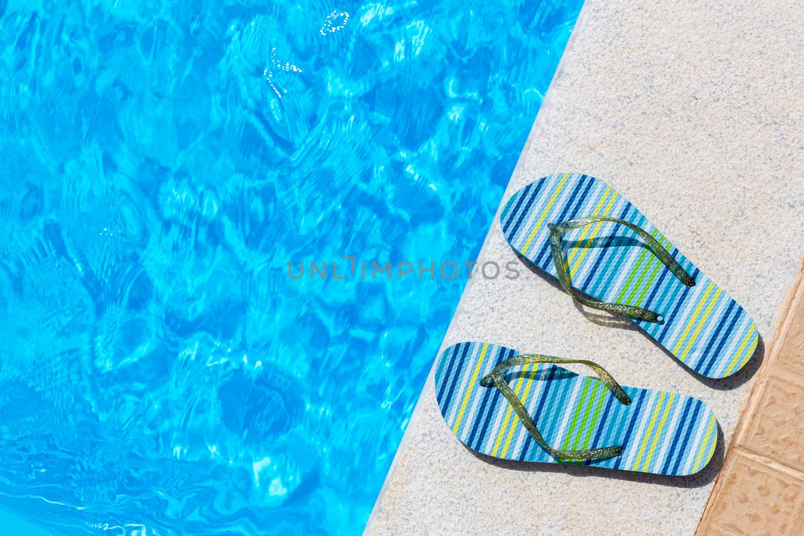 Pair of bathing slippers on edge of blue swimming pool