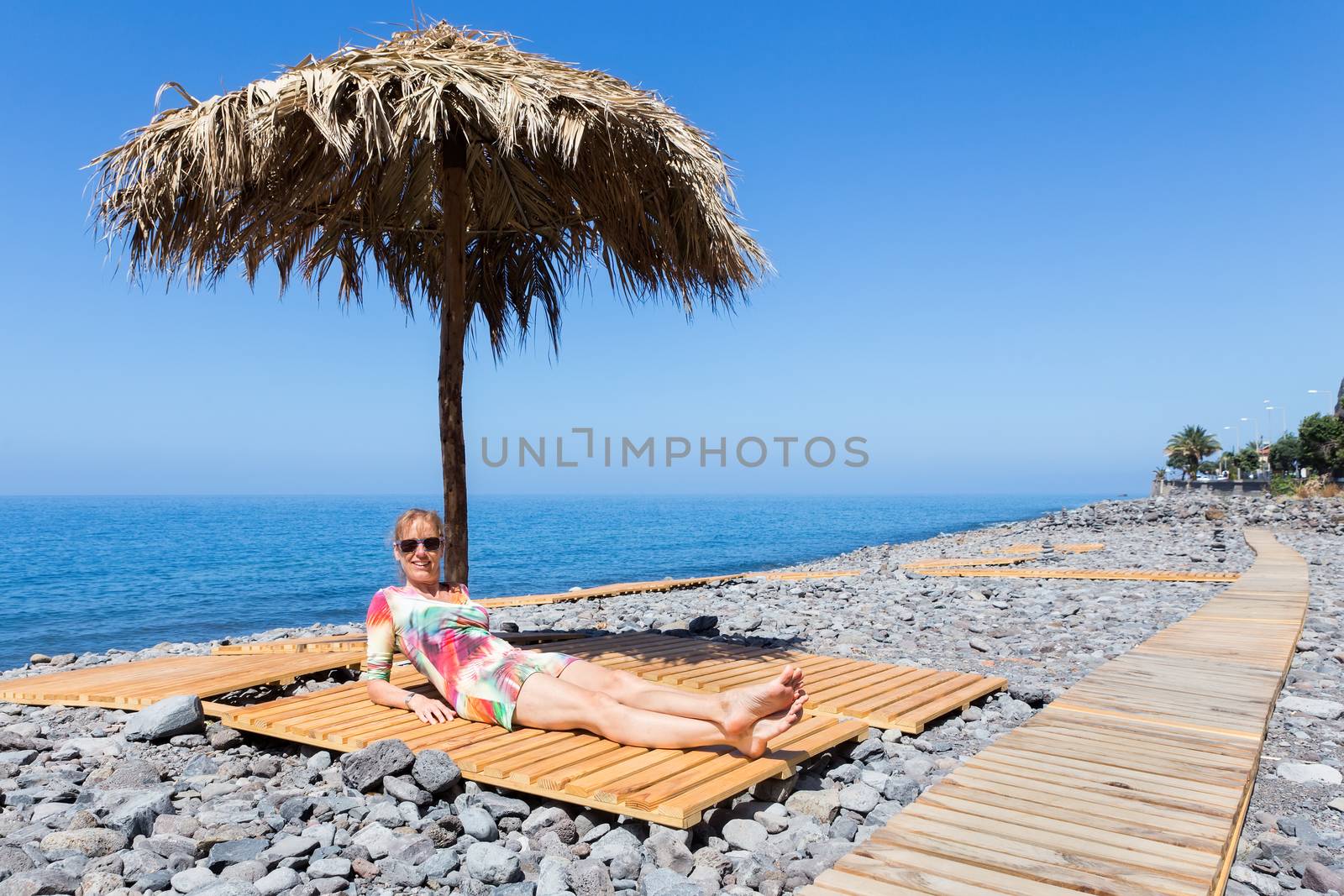 Woman sunbathing as tourist on stony portuguese beach by BenSchonewille