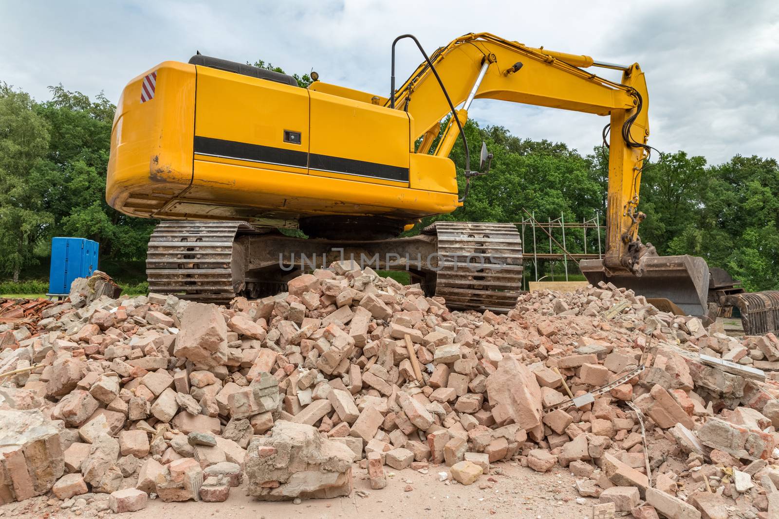 Yellow belt excavator on heap of bricks of demolished house
