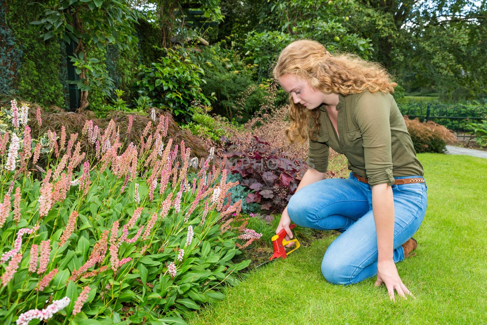 Young caucasian woman works in garden with grass shears