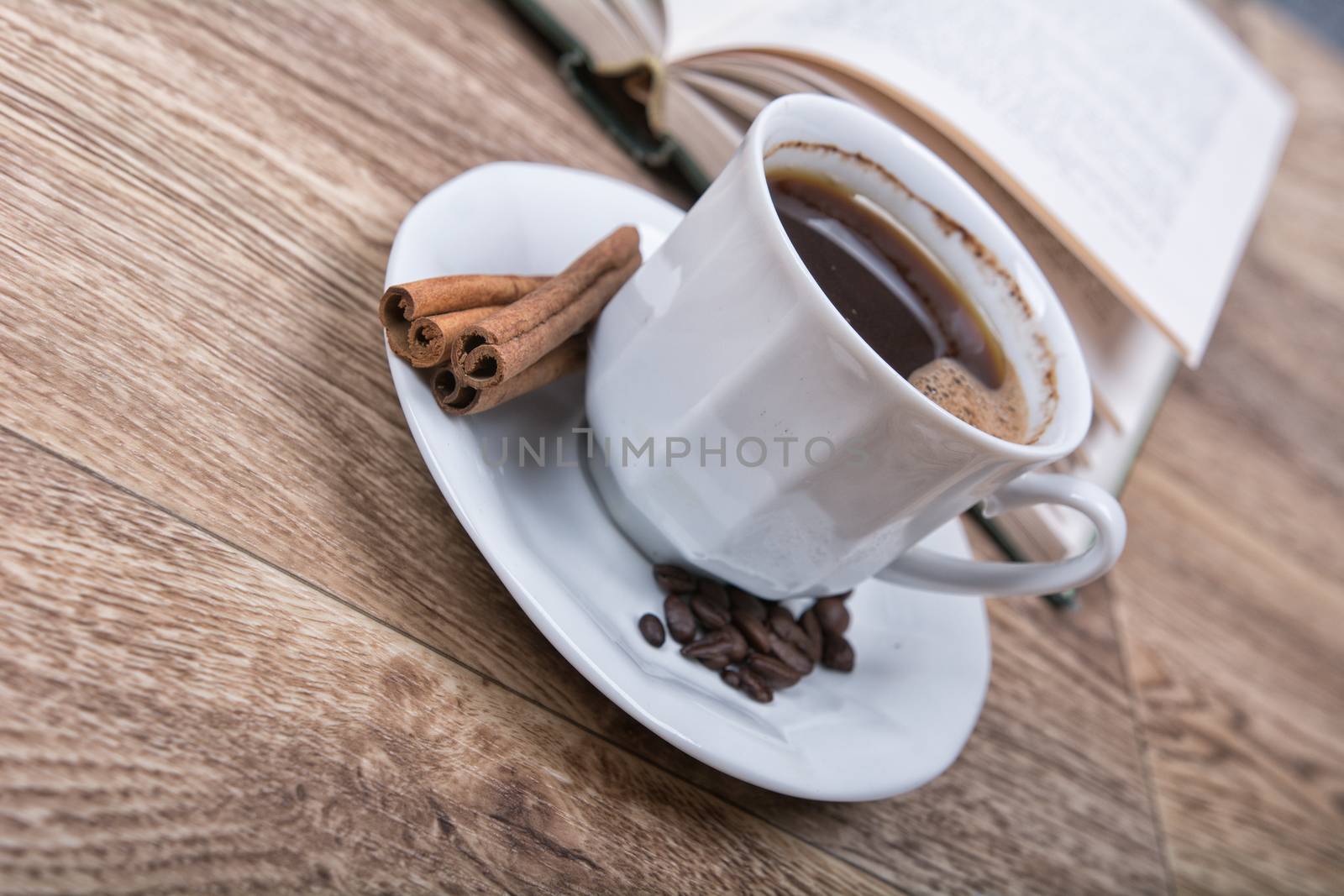 A cup of coffee and cinnamon with a book on a wooden background