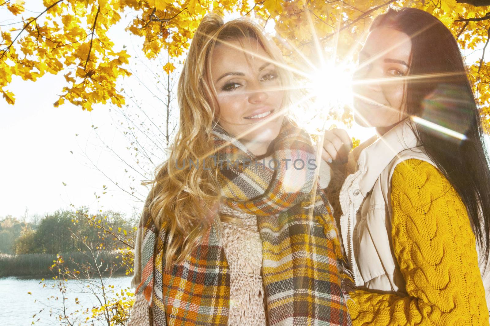 Two cheerful women in autumn park at sunny day