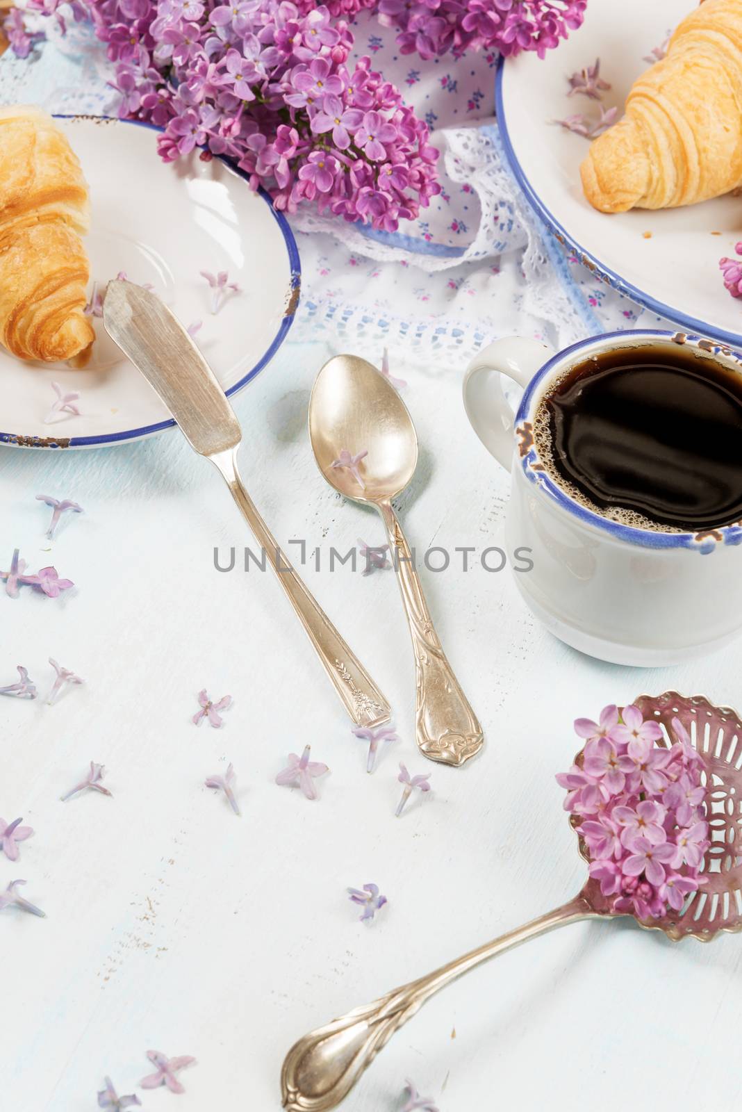 Spring breakfast with a cup of black coffee, croissants and lilac flowers